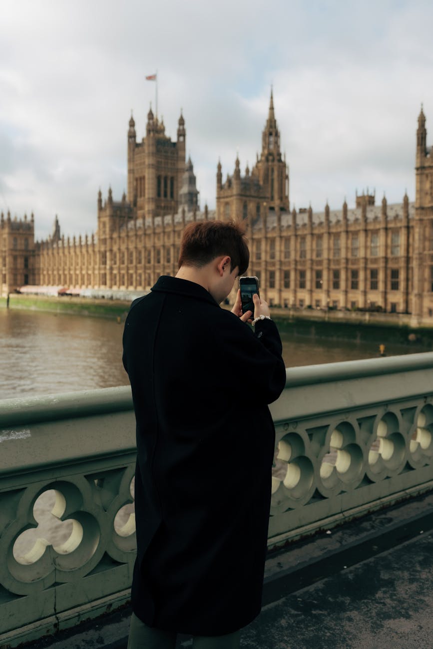 man in black coat taking pictures of westminster palace